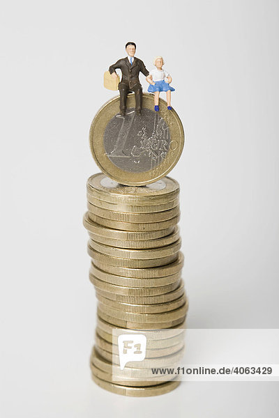 Figur eines Vaters mit Tochter sitzt auf einem Stapel Euro-Münzen  Symbolbild Familienkasse