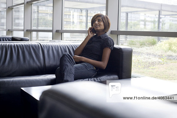 Junge dunkelhaarige Frau  Studentin  sitzt telefonierend auf einer Couch an einem Tisch