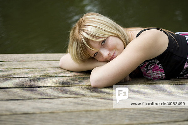 Junge blonde Frau liegt auf einem Steg am Wasser