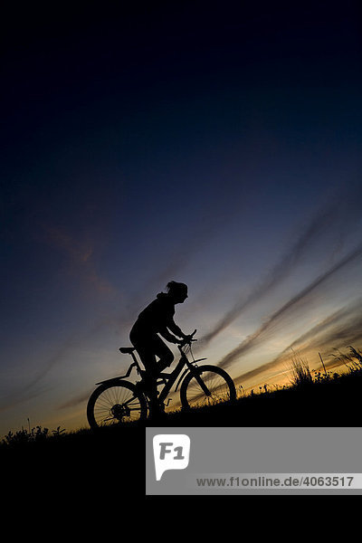 Young woman riding a bike  mountain bike  silhouette in front of evening sky