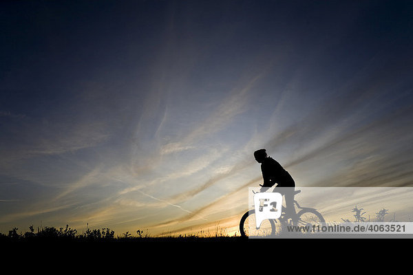 Junge Frau fährt Fahrrad  Mountain Bike  als Silhouette vor Abendhimmel