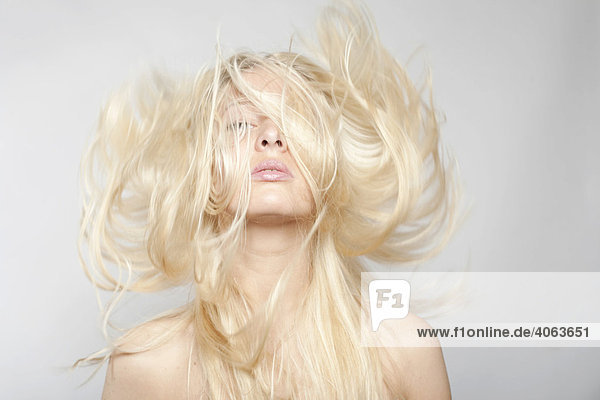 Junge blonde Frau mit fliegenden Haaren vor Grau