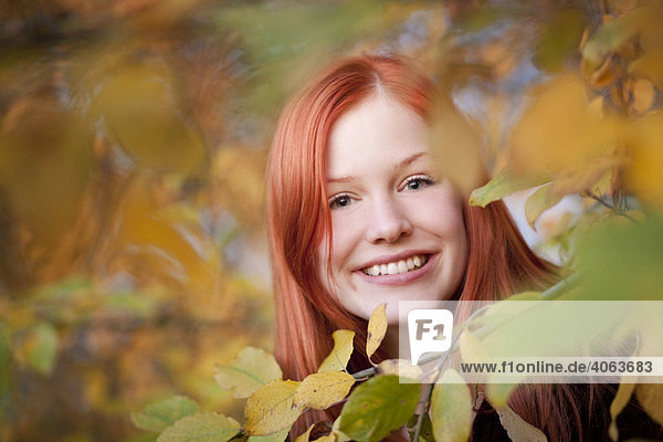 Portrait of a young red haired woman between autumnal leaves in a forest
