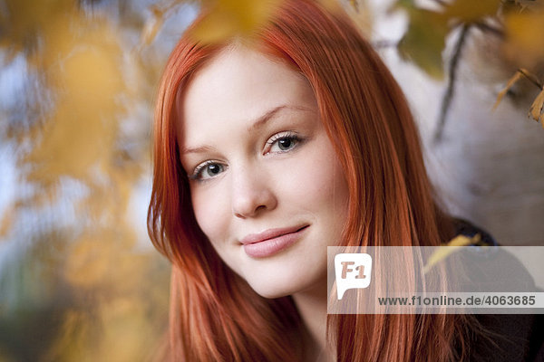 Portrait einer jungen rothaarigen Frau zwischen herbstlich gefärbten Blättern im Wald