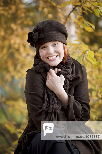 Young red haired woman wearing a woolen hat and scarf in an autumnal forest