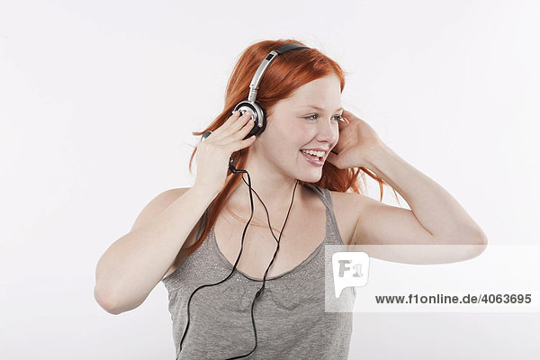 Young woman with long red hair listening to music on headphones