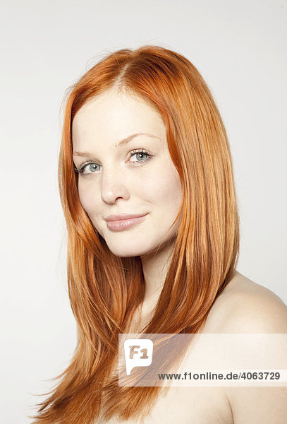 Portrait of a friendly smiling  young  red-haired woman in front of white backdrop
