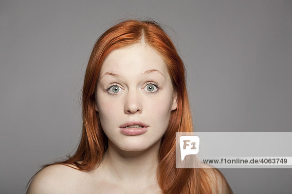 Surprised  young  red-haired woman looking into the camera