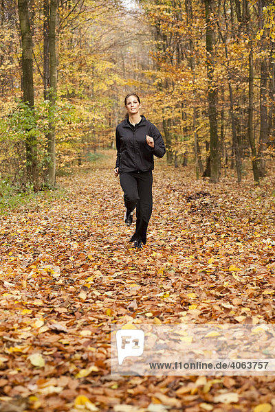 Junge dunkelhaarige Frau beim Fitnesstraining im Herbstwald