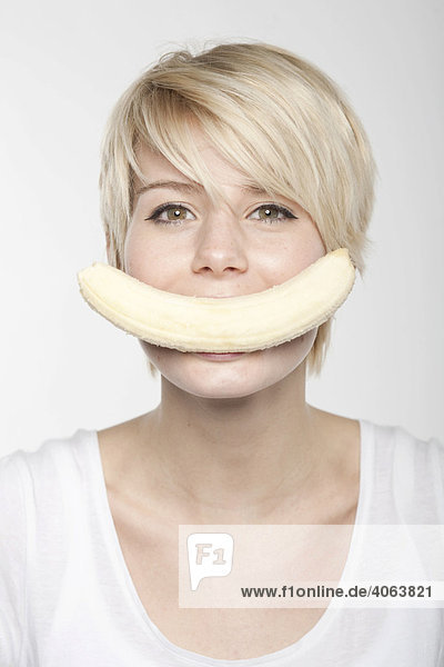 Junge blonde Frau mit kurzen Haaren hat eine Banane im Mund