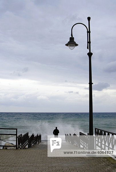 Young man standing at the edge of a pier looking out on a stormy sea  waves splashing  Amalfi Coast  Italy  Europe
