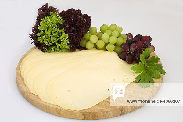 A block with diced Gouda  Dutch Cheese  on a wooden plank  with Lollo Rosso and Lollo Bionda  grapes and parsley
