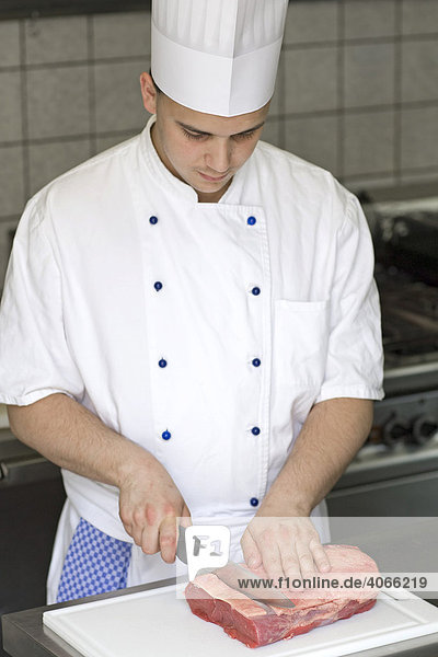 Junger Koch beim Portionieren eines Rinderroastbeefs zu Steaks