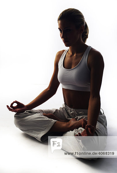Junge Kämpferin im Lotussitz macht Meditation  Gegenlichtaufnahme