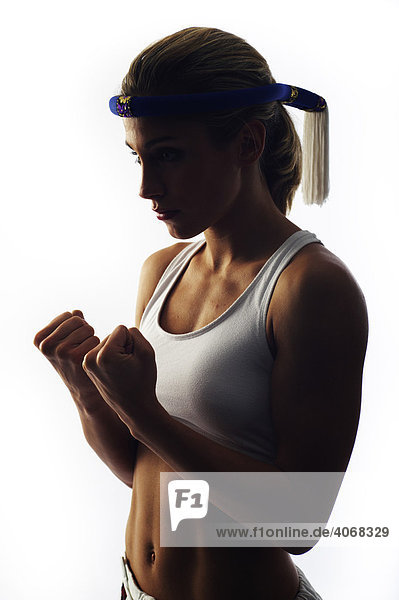 Young female fighter wearing a traditional Thai headband balling her fists  backlight