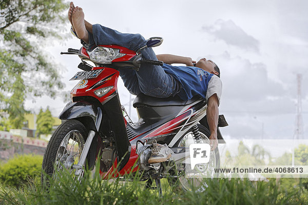 Young man lying on a moped  using his mobile  Putussibau  West Kalimantan  Borneo  Indonesia  Asia