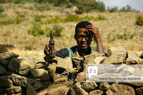 Boy standing behind a stone wall holding a holy figurine in his hand  Axum  Ethiopia  Africa