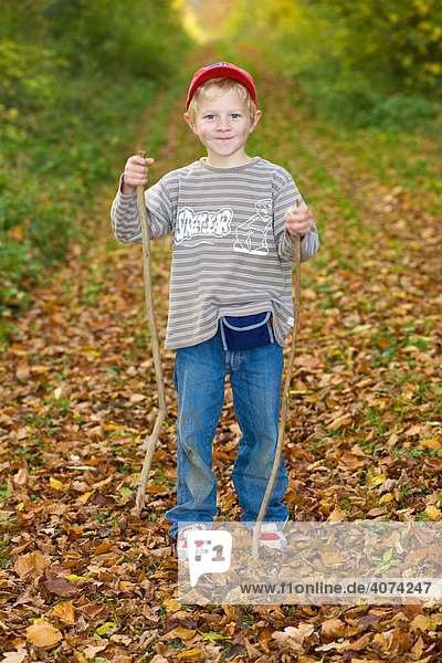Ein Junge  5 Jahre  mit zwei Wanderstöcken auf einem Waldweg