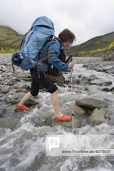Young woman  backpacker  hiker wading through a creek  St. Elias Mountains  Donjek Route  Kluane National Park  Yukon Territory  Canada  North America