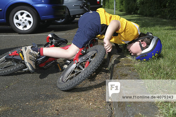 Five-year-old boy wearing a bicycle helmet falling off his bicycle  posed photo