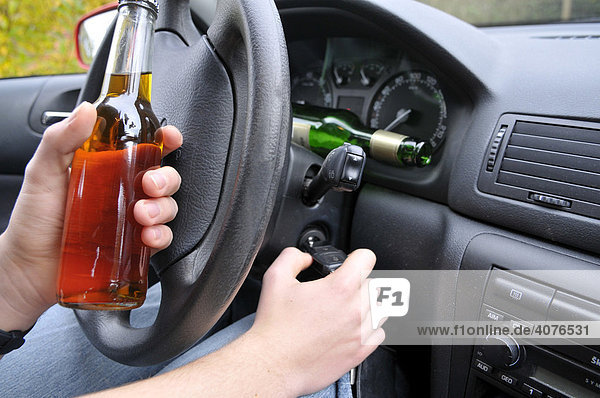 Hände eines Autofahrers mit Alkoholflasche am Steuer