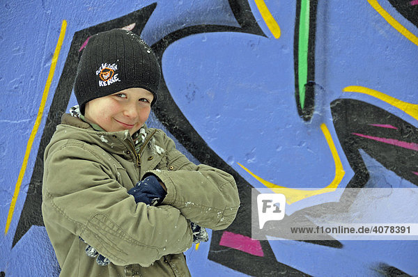 Ein achtjähriger Junge vor einer mit frischen Grafitti besprühten Wand an einem Bolzplatz in Köln  Nordrhein-Westfalen  Deutschland  Europa