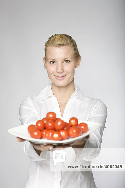 Junge Frau in weißer Bluse bietet Cocktailtomaten auf einem Teller an