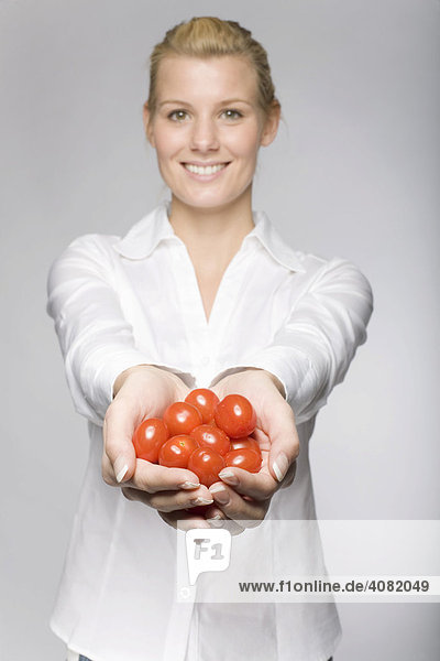 Frau in weißer Bluse hält viele Tomaten in beiden Händen