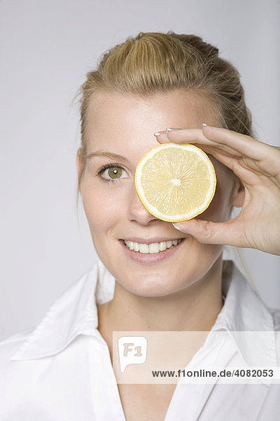 Junge Frau hält sich eine Zitronenscheibe vor ein Auge