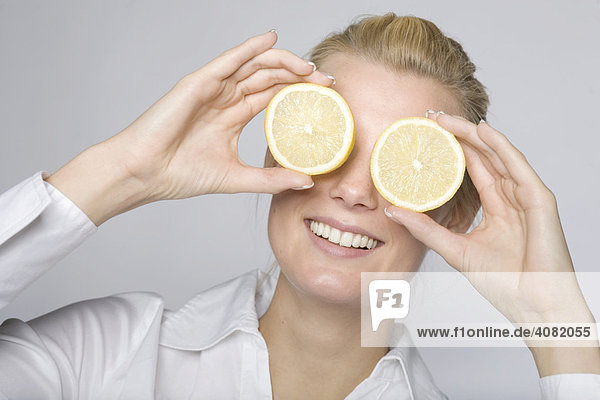 Junge Frau hält sich zwei Zitronenscheiben vor die Augen