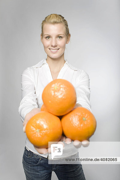 Blonde Frau hält drei Orangen und lacht