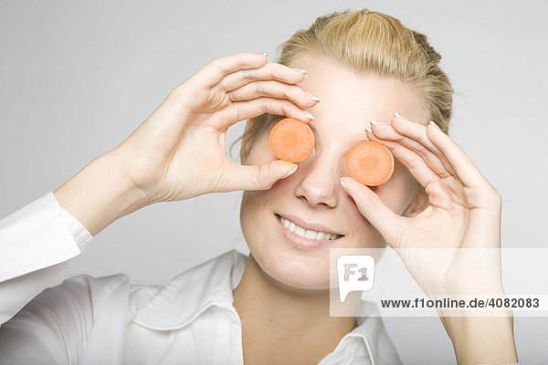 Junge blonde Frau hält sich zwei Karottenscheiben vor die Augen