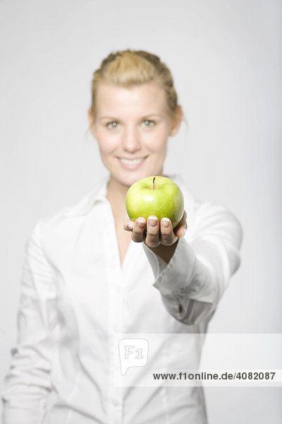 Junge blonde Frau hält einen grünen Apfel in Richtung Kamera