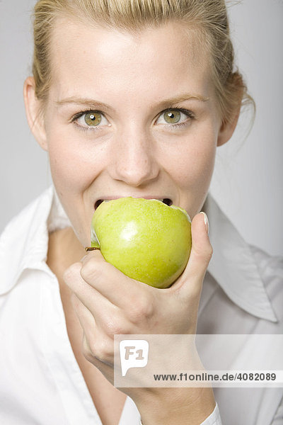 Junge blonde Frau beißt in einen grünen Apfel