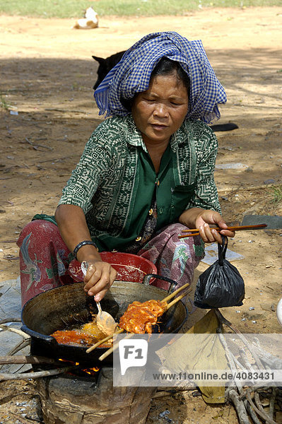 Frau mit Tuch auf dem Kopf grillt Fleischspieß Phnom Santuk bei Kompong Thom Kambodscha