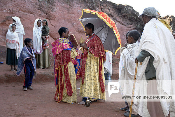 Ethiopian Orthodox Christianity priest reads out of the holy bible with believers in front of the rock hewn church Beta Marqorewos Lalibela Ethiopia