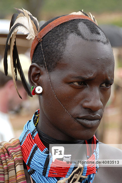 Portrait Junger Mann vom Volk der Banna mit Federn als Kopfschmuck und bunter Halskette auf dem Markt von Keyafer Äthiopien
