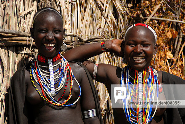 Zwei junge lachende Mädchen vom Volk der Arbore mit vielen bunten Halsketten vor einer Hütte Äthiopien