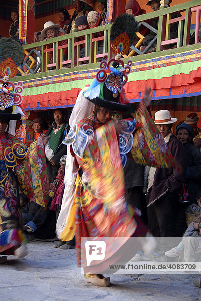 Blurred motion monk dances with fearful and mask and dress of a demon amongst many Tibetan pilgrims at festival in colourful decorated Rongbuk Monastery Tibet China