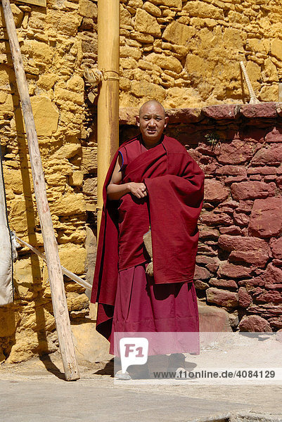 Tibetan monk stands at red and ochre painted wall Ganden Monastery Tibet China