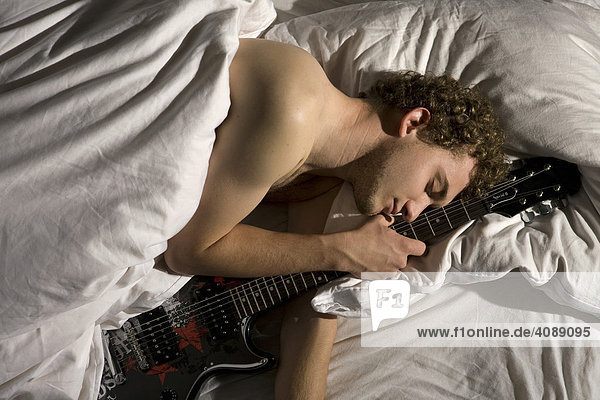 Junger Mann mit E-Gitarre im Bett