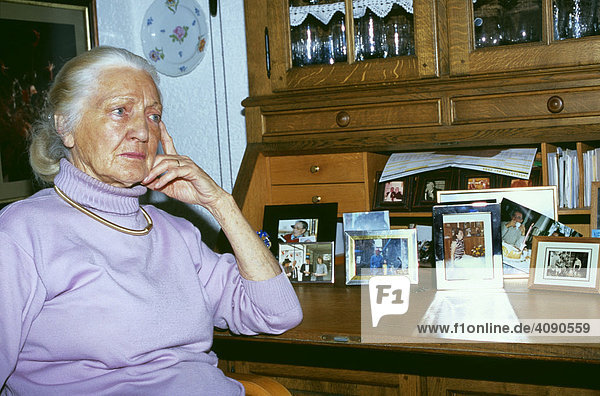 Alte Frau sitzt Gedankenversunken an einem Sekretär mit Familienbildern