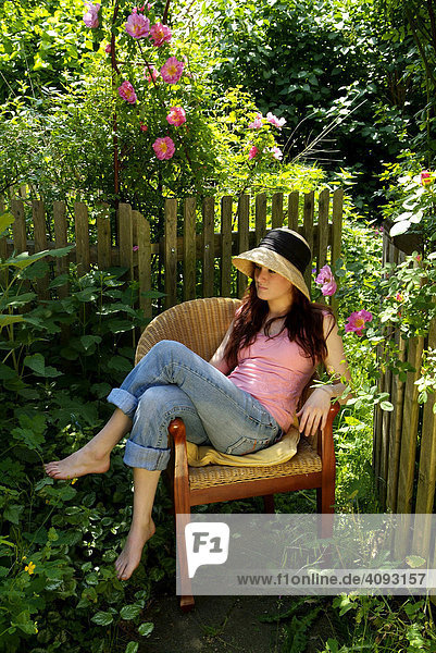 Junge Frau sitzt auf einem Stuhl im Garten und geniesst die Sonne