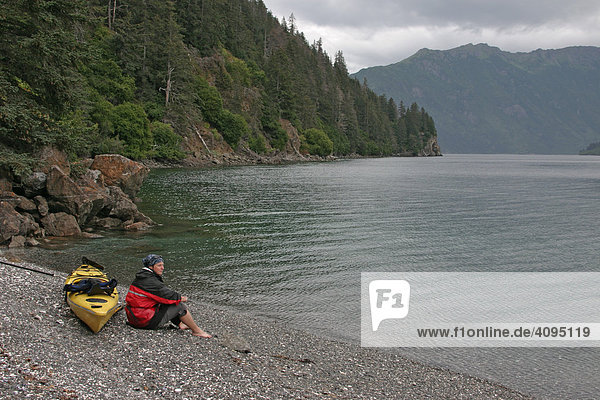 A woman with her sea Kayak rests in the solitude of the Otter Bay Alaska USA