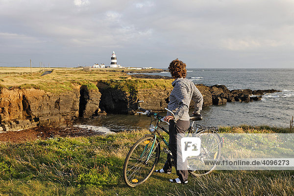 Radfahrerin blickt zum Leuchtturm am Hook¥s Head wo schon im 13. Jahrhundert ein Leuchtturm zu finden war  County Wexford  Irland