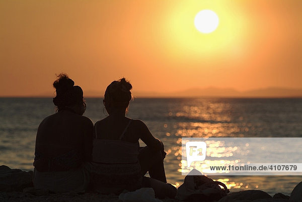 Two women on a beach watching the sunset over the ocean