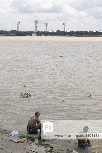 People bathing on the shore of Hooghly River  Ranji Stadium's floodlight towers  Howrah  Hooghly  West Bengal  India  Asia