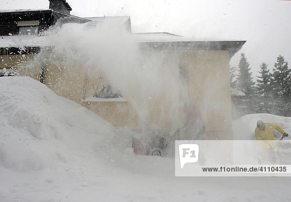Man moves the snow at his apartment house using an automatic snowblower in Oberwiesenthal  Erzgebirge  Erz Ore Mountains  Saxony  Germany
