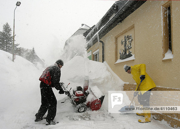 Männer räumen Schnee am Wohnhaus mit einer Schneefräsemaschine in Oberwiesenthal  Erzgebirge  Sachsen  Deutschland