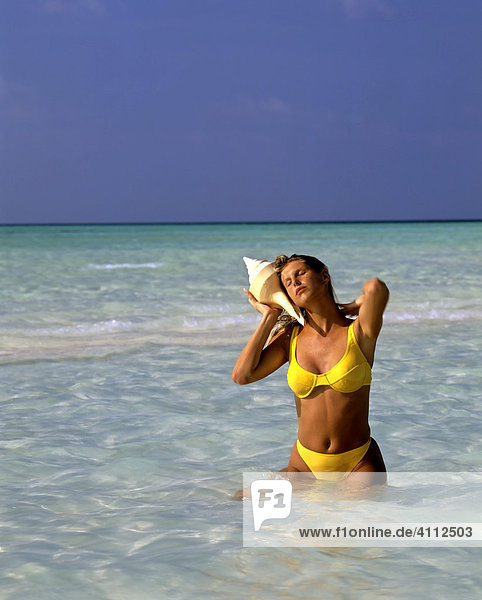 Young woman holding large shell to her ear  the sound of the ocean  Maldives  Indian Ocean